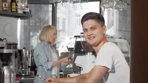 Bonito jovem sorrindo para a câmera enquanto desfruta de seu café no café — Fotografia de Stock