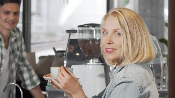 Kahve dükkanında bir fincan kahve aldıktan sonra kameraya gülümseyen genç kadın — Stok fotoğraf
