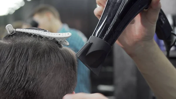 Cortado tiro de un peluquero usando secador de pelo mientras peina el cabello de un cliente — Foto de Stock