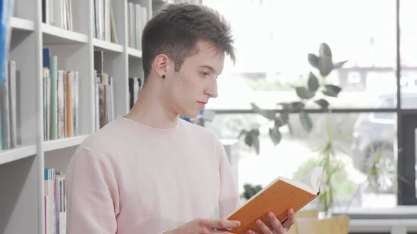 Young man enjoying reading a book at the library — Stock Photo, Image