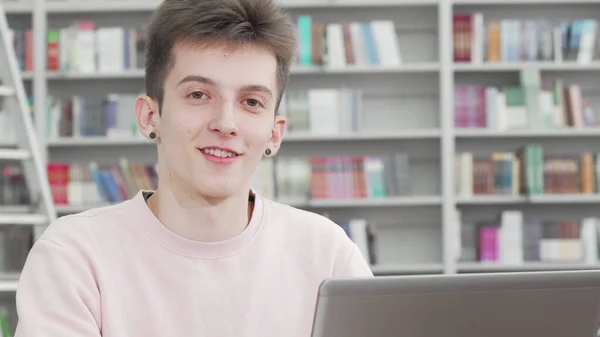 Tiro cortado de um jovem estudante sorrindo para a câmera na biblioteca — Fotografia de Stock