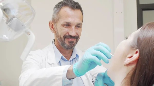 Ervaren mannelijke tandarts glimlachend tijdens het controleren van tanden van een patiënt — Stockfoto