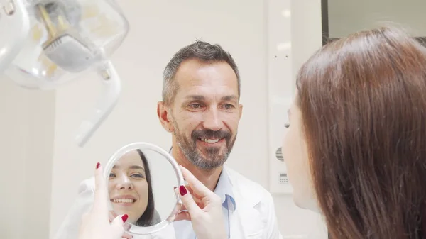 Szczęśliwy dojrzały dentysta rozmawia z pacjentem po badaniu lekarskim — Zdjęcie stockowe