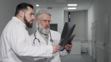 İki erkek doktor klinikte bir hastanın röntgen taramasını tartışıyor.