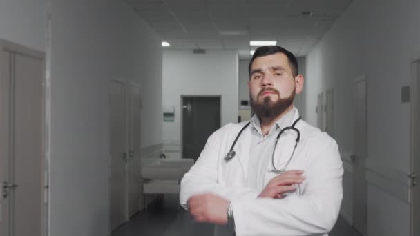 Zelfverzekerde jonge mannelijke arts glimlachend naar de camera in het ziekenhuis hal — Stockvideo