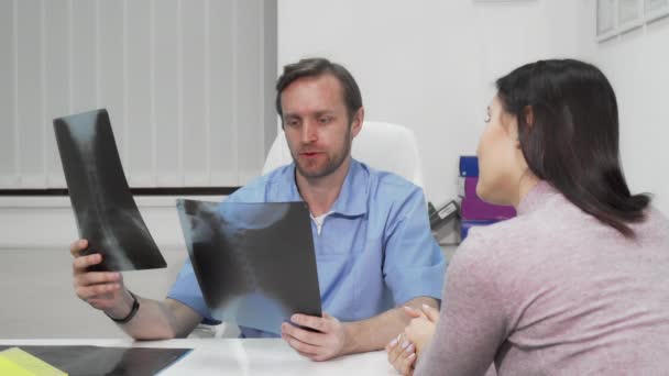 Volwassen mannelijke chirurg die röntgenscans van een vrouwelijke patiënt onderzoekt — Stockvideo