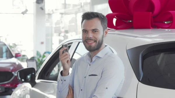 Attractive young man holding car keys to his new automobile at dealership