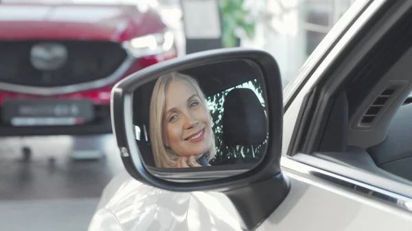 Hermosa mujer feliz sonriendo a la cámara a través del espejo lateral de su coche — Foto de Stock