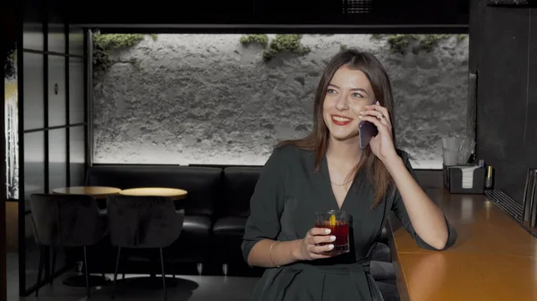 Beautiful woman talking on her phone while drinking cocktail at the bar