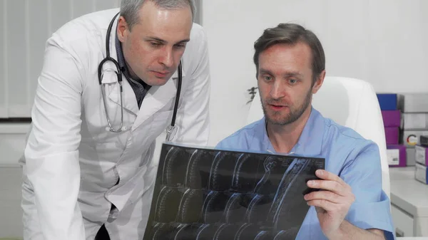 Зрелый хирург-мужчина просит совета у своего коллеги по МРТ пациента — стоковое фото