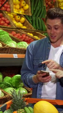 Enfes bir beyaz çift, canlı bir dizi taze ürünle çevrili akıllı bir telefondan alışveriş listeleriyle ilgili animasyonlu bir tartışmaya girişiyor. Havalı, ekose gömlekli, şık kızıl saçlı kadın, taze bir dolma biber seçiyor.