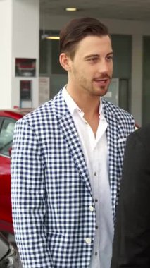 Modern bir araba galerisinde, keskin kareli ceketli memnun bir alıcı profesyonel bir satıcıyla el sıkışır ve heyecan verici araba anlaşmalarını sonuçlandırır. Işıldayan araçlarla dolu canlı sergi salonu,