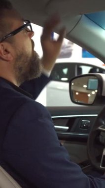 Modern bir galeride araba anahtarını elinde tutan gözlüklü, şık sakallı, gururlu bir adam. Kendine güvenen gülüşü ve özel kıyafeti heyecan saçıyor. Seyircileri yeni otomotiv alımının heyecanını paylaşmaya davet ediyor.