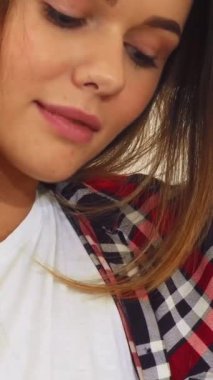 Yumuşak ışıklı, rahat bir odada, koyu saçlı genç bir kadın pofuduk bir koltukta oturuyor, sıcak gülümsemesi pozitiflik saçıyor. Rahat duruşu ve büyüleyici ifadesi, izleyicileri sakin hayal dünyasına ve mutlu düşüncelerine davet ediyor.