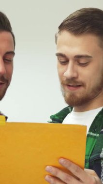 Canlı bir kütüphanede, iki genç adam canlı sarı bir klasörden dokümanları incelerken yüzleri kahkahalarla parlıyordu. Bu neşeli arkadaşlık anı, renkli rafların arasındaki bağlantılarını gösteren pozitifliği yansıtıyor.