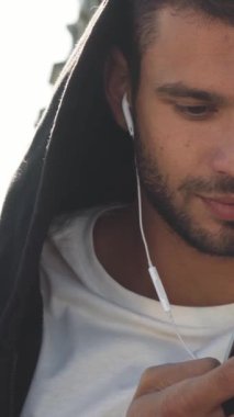 Koyu saçlı ve sakallı neşeli bir genç adam bir bankta oturuyor, telefonuyla meşgul bir şekilde mesajlarına cevap veriyor. Onun ışıl ışıl gülüşü canlı bir şehir zemininde parlıyor, şehrin canlı özünü ve modern neşesini yakalıyor.