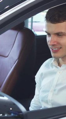Şık, modern bir arabanın direksiyonunu sıkıca kavrayan koyu renk saçlı, heyecan dolu neşeli genç bir adam. Zengin deri ve modern teknolojiyle donatılmış lüks iç mekan, izleyicileri heyecan verici bir otomotife davet ediyor.