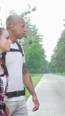 Maceracı, çok ırklı bir çift, huzurlu bir kırsal yolda başparmakları havada bir gezinti için sabırsızlıkla bekliyor. Canlı sırt çantaları ve ışıltılı gülümsemeleriyle, keşif ve neşe ruhunu somutlaştırırlar, ilerideki yolculuğu kucaklamaya hazırdırlar.