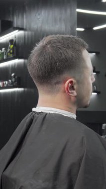 Şık, modern bir berber dükkanında, yetenekli bir berber, erkek müşterisi için ayna tutar, erkek müşterisi de onun yeni ve şık saç kesimine hayrandır. Titreşimli atmosfer, her ayrıntının katkı sağladığı tımarcılığın sanatsallığını vurguluyor.