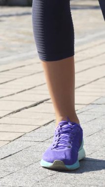 Açık tenli genç bir kadın, güzel bir nehir yürüyüşünde bacaklarını enerjik bir şekilde açar ve güneşin altında güneşlenir. Şık mor spor ayakkabıları ve dar taytları dinamik hareketler arasında akıcı bir şekilde geçiş yaparken atletik formunu vurguluyor.