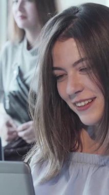 Hoş bir kafede dizüstü bilgisayarı üzerinde çalışırken canlı bir görüntülü konuşma yapan dalgalı saçlı çekici bir kadın ışıl ışıl gülümsüyor. Yumuşak doğal ışık ve sohbetin hafif uğultusuyla dolu ılık bir ortam,