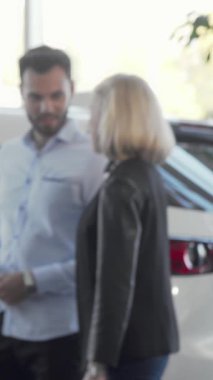 Neşeli bir çift, ışıldayan araçlar ve çarpan kırmızı bir fiyonk ile çevrili canlı bir araba galerisinde şık bir otomobili zevkle inceliyor. İfadeleri heyecan ve heyecan saçar ve önlerindeki heyecanlı yolculukları hayal ederler.