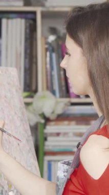 Dalgalı saçları ve canlı kırmızı bir bluzu olan odaklanmış genç bir kadın, kendini sanatına kaptırıyor, rahat bir sanat atölyesinde tuvalinin renklerini ustalıkla harmanlıyor. İlham verici bir dizi sanat malzemesi ve kitapla çevrelenmiş halde, yaratıcılığını yayıyor ve