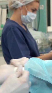 Temiz bir cerrahi ortamda, odaklanmış bir hemşire nazikçe doktorun eline sterilize bir eldiven takar ve güvenlik ve hijyenin önemini vurgular. Bu samimi an tıbbi ekibin sarsılmaz bağlılığını ve takım çalışmasını gözler önüne seriyor.