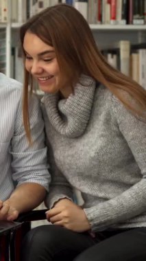 Genç sakallı bir adam ve büyüleyici kahverengi saçlı bir kadın, rahat bir kütüphanedeki parlak bir dizüstü bilgisayarın eğlenceli bir videosunun keyfini çıkarırken kahkahalara boğuldular. Renkli kitaplıklarla dolu yüksek kitaplıklarla çevrelenmiş neşeli bağlantıları bir davet yaratıyor.