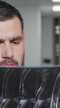 Kendini işine adamış beyaz önlüklü bir erkek doktor yoğun bir konsantrasyonla MRI taramasını inceler ve hastanın sağlığına olan bağlılığını yansıtır. Pürüzsüz, modern hastane arkaplanı profesyonelliğin atmosferini yükseltiyor.