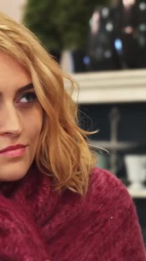 Yumuşak, dalgalı sarı saçlı genç bir kadın görkemli pembe bir battaniyenin içine yerleşir, sıcaklık ve rahatlık saçar. Onun huzurlu ifadesi ve nazik gülümsemesi, şık dekore edilmiş bir odada rahatlamak için mükemmel bir ortam yaratıyor.