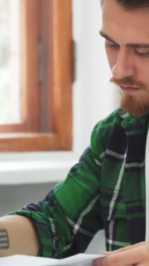 Koyu renk saçlı ve şık sakallı kendini adamış genç bir adam, yoğun bir şekilde, edebiyat yığınlarıyla çevrili, güneşli bir sınıfta kitap okuyor. Camdaki sıcak parıltı, onun düşünceli ifadesini vurguluyor, akademik takibin özünü yakalıyor.