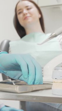 Canlı önlük giymiş odaklanmış bir erkek dişçi, sakin bir kadın hastanın dişlerini ayrıntılı diş kalıbı ve parlak aletleriyle özenle inceler. Bu klinik sahne profesyonelliği ve güveni yansıtıyor.