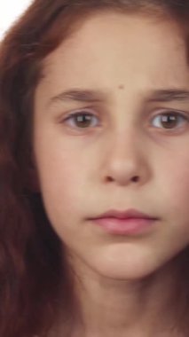 Bu büyüleyici kız, kıvırcık siyah saçları yüzünün etrafında şelale gibi dalgalanan, sessiz kalmak için parmağını dudaklarına dayayarak sinyal veriyor. Geniş, anlamlı kahverengi gözleri, yumuşak beyaz arka plana karşı merakla parıldıyor.