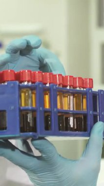 Üst düzey teknolojilerle dolu parlak bir laboratuvarda koruyucu eldiven ve gözlük takmış genç bir laboratuvar çalışanı renkli numunelerle dolu canlı test tüplerini inceliyor. Yoğun odaklanması ve hassasiyete olan bağlılığı