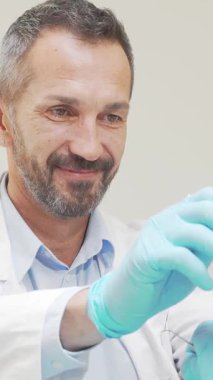 Gıcır gıcır beyaz bir ceket ve mavi eldivenlerle süslenmiş yetenekli bir erkek dişçi, parlak, modern bir klinikte tanınmayan bir kadının dişlerini dikkatle incelerken sıcaklıkla ışıldıyor. Dostça tavrı ve profesyonel yaklaşımı güven verici.