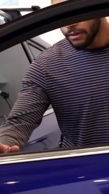 Gösterişli, modern bir sergi salonunda çarpıcı bir mor geçidin kapısını hevesle açan şık, genç bir siyah adam neşeyle parıldıyor. Baş parmakları ve ışıl ışıl gülüşü, yeni sahibini kucaklamanın coşkulu anını yakalıyor.