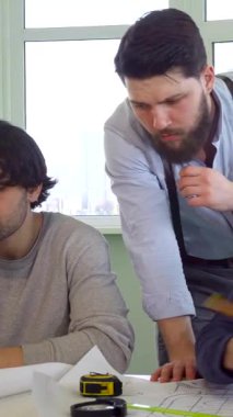 Güneşli bir ofiste, genç erkek mimarlardan oluşan dinamik bir ekip projeleri için yenilikçi çözümler üretiyor. Siyah kazaklı sakallı esmer mühendis meslektaşlarına rehberlik ederken çekici Kafkasyalı baş tasarımcı...