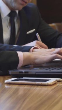 Bu yakın çekim gösterilerinde bir iş kadını ellerini parlak bir dizüstü bilgisayarın üzerinden uçururken, keskin takım elbiseli bir işadamı onun yanına özenle notlar yazıyor. Parlak ahşap masanın sıcak tonları ve ortam aydınlatmasının yumuşak parıltısı bir ışık yaratıyor.