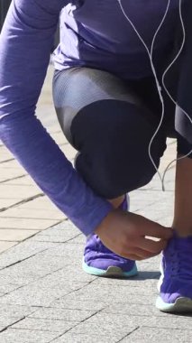 Kararlı genç bir kadın güneşli bir nehir kıyısında, göz alıcı mor spor ayakkabılarının bağcıklarını ustalıkla bağlıyor. Odaklanmış bakışları ve atletik kıyafetleriyle canlandırıcı bir açık hava macerasına hazırlanıyor. Enerji ve stili somutlaştırıyor.