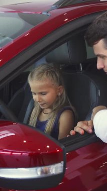 Kendini adamış bir baba açık pencereden sarkmış, kızına arabalarda rehberlik ediyor ve kızına direksiyon başında güvenle oturuyor. Canlı araba galerisindeki neşeli değişimleri sıcaklık ve bağlantı yayarak değerli bir şeyi yakalıyor.