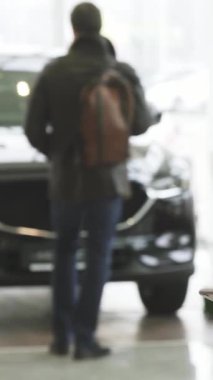 Şık sakallı genç bir adam akıllı telefonuyla özümsenmiş halde duruyor. Çağdaş bir araba galerisindeki lüks araçların cazibesiyle kolayca harmanlanan bir teknoloji. Bu dinamik sahne, dijital ortamda modern tüketiciliğin heyecanını yayıyor.