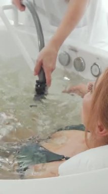 Sakinleştirici bir girdap banyosunda lüks içinde, vücudunu ve ruhunu canlandıran bir hidromasaj zevkini çıkaran bir kadının sakin arka görüntüsü. Yumuşak su kabarcıkları ve yumuşak ortam aydınlatmasıyla vurgulanan sakin spa atmosferi, cennet gibi bir ışık yaratıyor.