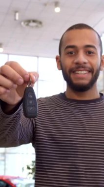 Zevkli bir Afro-Amerikalı adam, şık araçlarla dolu parlak ve modern bir galeride duran parlak bir araba anahtarını elinde tutarken gururla ışıldıyor. Davetkar atmosfer heyecan ve memnuniyet yayar.