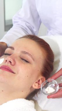 Kendini adamış beyaz önlüklü bir kozmetik uzmanı müşterisinin yüzüne nazikçe lüks bir krem sürerek doğal güzelliğini uzman hassasiyetiyle arttırıyor. Bir elinde narin bir fırça, diğer elinde küçük bir kâse, güzellik uzmanı