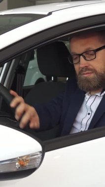 Şık sakallı ve gözlüklü sofistike olgun bir erkek müşteri, bayilikte modern bir arabanın gösterişli iç mekanını keşfetmekle son derece meşgul. Rahatça oturur, direksiyona hafifçe dokunur, heyecan saçar ve...