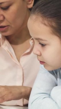 Bu dokunaklı yakın çekim, meraklı kızına kitap sayfalarında rehberlik eden Asyalı bir annenin sıcacık bir kütüphanenin parıltısıyla aydınlanan yüzlerini gösteriyor. Sahne öğrenmenin hazzını ve derin bağları özetliyor.