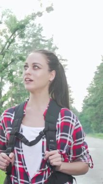 Neşeli, çok kültürlü bir çift sakin bir kırsal yolda otostop çekmeye ve keşfin heyecanını kucaklamaya hazır. Canlı sırt çantaları ve parlak gülümsemeleri yemyeşil ve açık gökyüzündeki yolculuklarının heyecanını yansıtıyor.