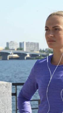 Neşeli genç bir kadın nehir kıyısında güven içinde duruyor, kameraya parlak bir gülümseme göstermeden önce saatine bakıyor. Uzun siyah saçları at kuyruğu ve canlı mor bir bluzu ile güneşli bir şehre karşı mutluluğu somutlaştırıyor.