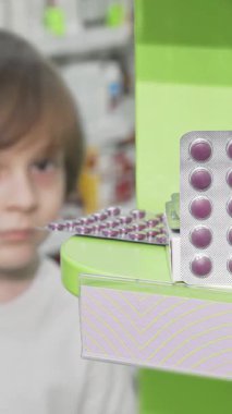 Neşeli küçük bir çocuk neşeli bir gülümseme ile ilginç bir şekilde sağlıklı ürünlerle dolu raflarla çevrili canlı bir eczanede renkli su toplayan hapları inceliyor. Bu büyüleyici sahne çocukluk merakının ve neşesinin özünü yakalıyor.